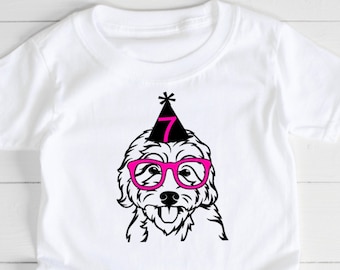 Puede incluir: Camiseta blanca con una ilustración en blanco y negro de un perro con gafas rosas y un gorro de fiesta con el número 7. El diseño está centrado, adecuado para un cumpleaños infantil. La camiseta es de algodón.