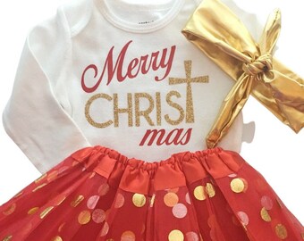 May include: A baby Christmas outfit set featuring a white long-sleeve bodysuit with "Merry CHRISTmas" in red and gold glitter lettering. The set includes a red tutu skirt with gold polka dots and a gold headband.