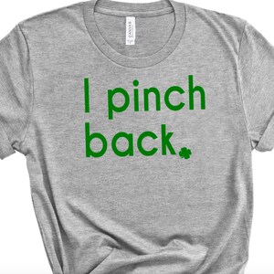 May include: A heather gray t-shirt with the text "I pinch back" in green, along with a green shamrock. The shirt has rolled-up sleeves and a crew neck. The shirt is made of a soft material.