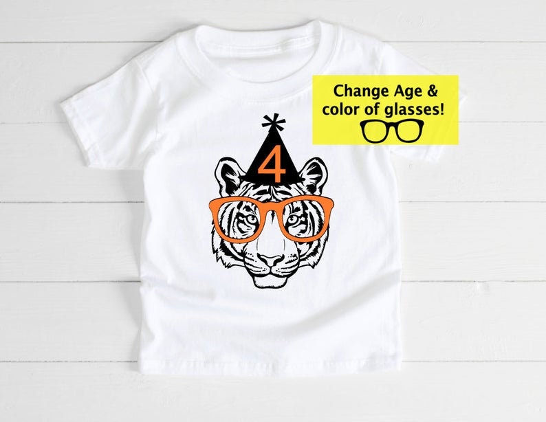 May include: White t-shirt featuring a tiger face wearing orange glasses and a black party hat with the number 4. The text "Change Age & color of glasses!" is in a yellow box. A fun birthday shirt.