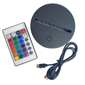 Puede incluir: Una base LED negra con un bot&oacute;n de encendido, un mando a distancia con opciones de color y un cable USB. El mando tiene botones para la selecci&oacute;n de color, brillo y efectos especiales como estrobosc&oacute;pico y fundido. La base es redonda.