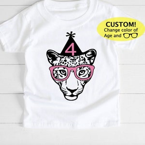 May include: White t-shirt featuring a leopard face wearing pink glasses and a party hat with the number 4. The text "CUSTOM! Change color of Age and" is in a yellow oval on the right side of the shirt.