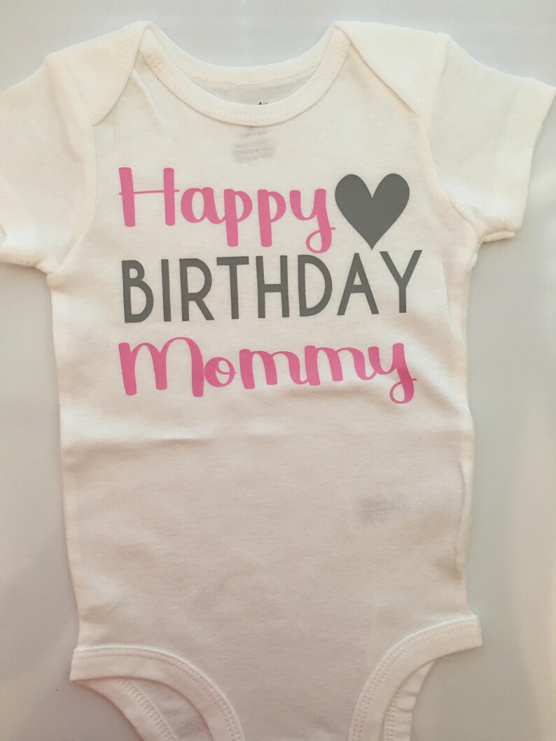 May include: White baby onesie with the text "Happy Birthday Mommy" in pink and gray lettering, with a gray heart graphic. The onesie has short sleeves and a simple design.