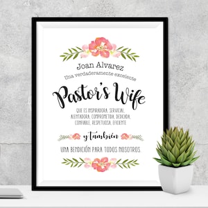 May include: A framed print with a floral design and the text "Joan Alvarez Una verdaderamente excelente Pastor's Wife QUE ES INSPIRADORA, SERVICIAL. ALENTADORA, COMPROMETIDA, DEDICADA, CONFIABLE, RESPETUOSA, EFICIENTE y tambi&eacute;n UNA BENDICI&Oacute;N PARA TODOS NOSOTROS."