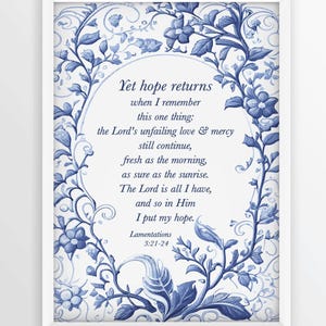 Puede incluir: Una impresión enmarcada con borde blanco presenta un diseño floral azul y blanco que rodea un óvalo central. El óvalo contiene texto de Lamentaciones 3:21-24, incluyendo "Yet hope returns" y "I put my hope."