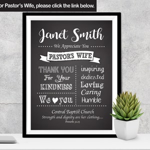 May include: Black and white chalkboard sign with the text "Janet Smith" and "Pastor's Wife". The sign also includes the text "Thank You" and "We Love You" with a heart symbol. The sign is framed in a black frame and is sitting on a table with a small potted plant.