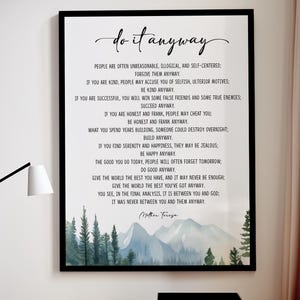 May include: Black framed art print with the quote "do it anyway" by Mother Teresa. The print features a watercolor landscape of mountains and trees at the bottom. The text is in a stylish, handwritten font.