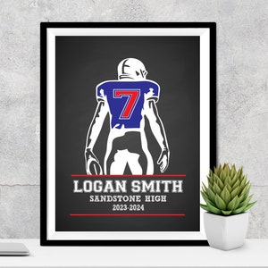 Puede incluir: Impresi&oacute;n enmarcada de un jugador de f&uacute;tbol americano con uniforme azul y blanco, n&uacute;mero 7. El jugador sostiene un bal&oacute;n. La impresi&oacute;n incluye el nombre "LOGAN SMITH", "SANDSTONE HIGH" y el a&ntilde;o "2023-2024" en texto blanco sobre fondo negro.