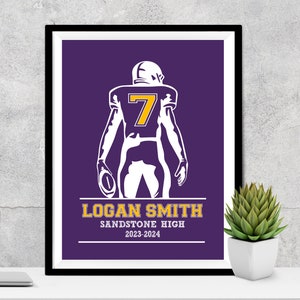 Puede incluir: Impresi&oacute;n enmarcada de un jugador de f&uacute;tbol americano con uniforme morado y el n&uacute;mero 7 en dorado. El jugador sostiene un bal&oacute;n de f&uacute;tbol. La impresi&oacute;n incluye el nombre "LOGAN SMITH", "SANDSTONE HIGH" y el rango de a&ntilde;os "2023-2024".