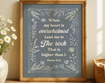 May include: A framed print with a wooden frame. The print has a blue background with white text and floral border. The text reads "When my heart is overwhelmed, Lead me to The rock That is higher than I. Psalm 61:2."