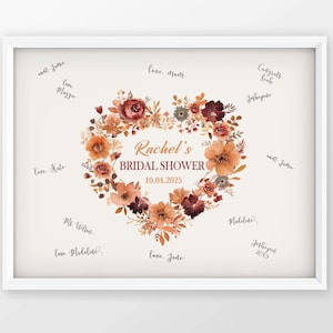 May include: A framed print with a floral heart design, featuring the text "Rachel's Bridal Shower 10.04.2025." The heart is composed of orange, brown, and burgundy flowers. Handwritten messages surround the heart.
