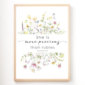 May include: A framed print featuring a watercolor floral arrangement in shades of yellow, pink, and purple. The text "She is more precious than rubies" is displayed in elegant script, with the Bible verse Proverbs 3:15 below.