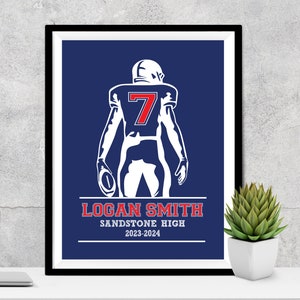 Puede incluir: Impresi&oacute;n enmarcada de un jugador de f&uacute;tbol americano con uniforme blanco y el n&uacute;mero 7 en rojo. El jugador sostiene un bal&oacute;n sobre un fondo azul. La impresi&oacute;n incluye el nombre "LOGAN SMITH" y "SANDSTONE HIGH 2023-2024".