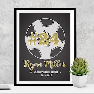 May include: Black and white soccer ball with a gold number 24 on it. The text "Ryan Miller" is below the ball, and the text "Sandstone High 2019-2020" is below that.