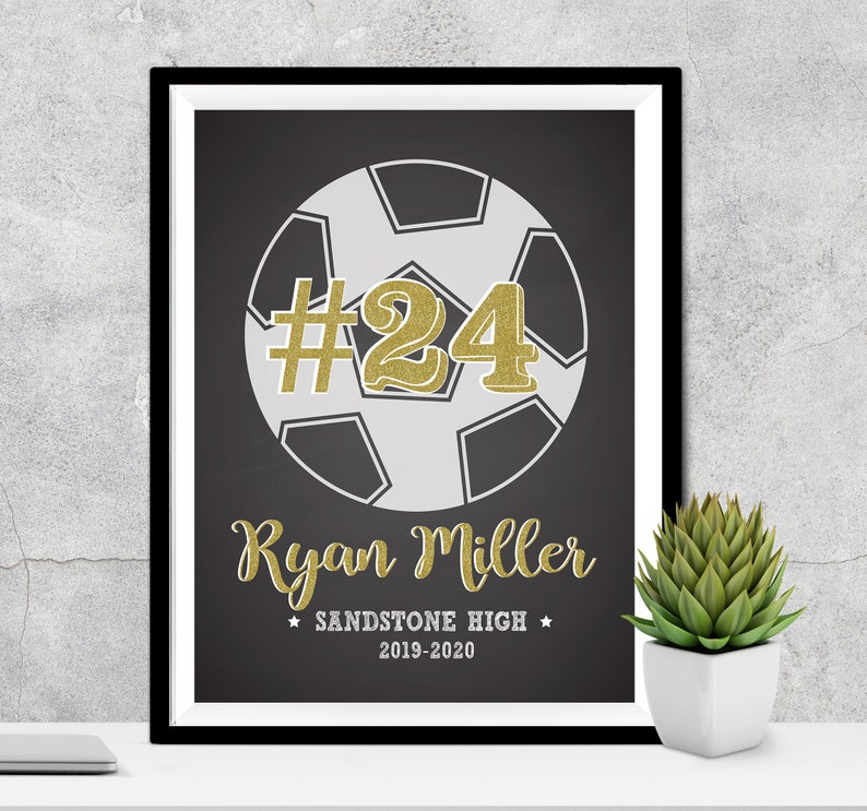 May include: Black and white soccer ball with a gold number 24 on it. The text "Ryan Miller" is below the ball, and the text "Sandstone High 2019-2020" is below that.