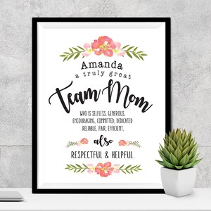 May include: A framed print with the text "Amanda a truly great Team Mom" in black script. The print includes floral and leaf accents in pink and green. Additional text describes qualities like selfless, generous, and helpful.