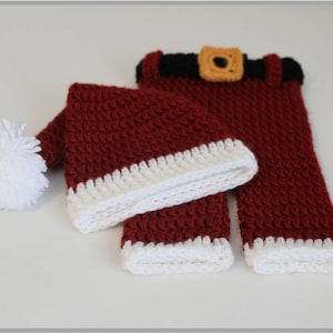 May include: A red and white crocheted Santa hat with a white pom-pom and matching red and white crocheted pants with a black belt and a yellow buckle.