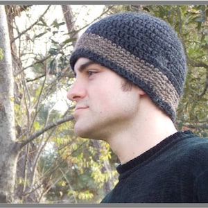 May include: A dark gray and brown crocheted beanie with a wide brim. The beanie is worn by a person with a light complexion and short brown hair.