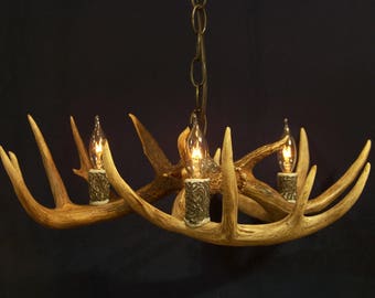 Può includere: Un lampadario fatto di corna di cervo con tre lampadine. Le corna sono di colore marrone naturale e le lampadine sono di vetro trasparente.