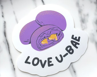 Puede incluir: Una pegatina blanca con una ilustración morada y amarilla de un pastel de ube halaya. El texto "LOVE U-BAE" está escrito en negro debajo del pastel.