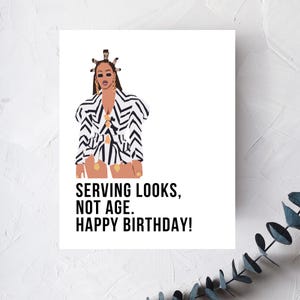 May include: A white greeting card with a fashion illustration of a person in a black and white zig-zag patterned outfit. The text reads: "SERVING LOOKS, NOT AGE. HAPPY BIRTHDAY!"