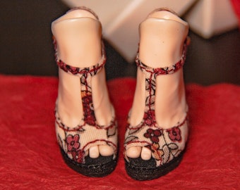 May include: A pair of floral patterned heeled sandals with a t-strap design. The sandals are a light beige color with red, pink, and green floral accents. The heels are black.