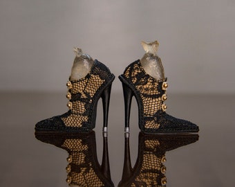 May include: A pair of black lace high-heeled shoes with gold buttons. The shoes are reflected in a shiny surface.