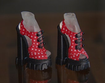 May include: A pair of red and white polka dot platform heels with black laces and buckles. The heels are made of a black fabric and have a chunky platform.