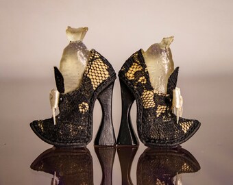 May include: A pair of black lace high-heeled shoes with a unique design. The heels are tall and have a curved shape. The shoes have a bow on the front and a clear plastic detail on the top.