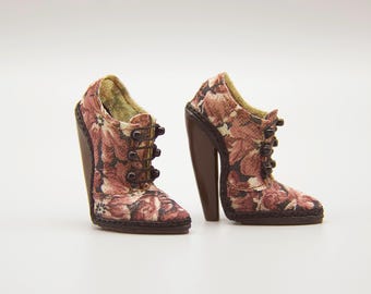 May include: A pair of high-heeled shoes with a floral pattern in shades of red, pink, and brown. The shoes have dark brown heels and button details. The interior lining is a golden color.