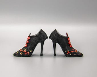 May include: A pair of black high-heeled shoes with red and floral embroidery. The shoes have a pointed toe and a lace-up design.