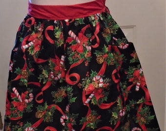 May include: A Christmas-themed apron with a black background. The apron features a red waistband and is decorated with red ribbons, candy canes, holly, and pinecones. The apron has two pockets.