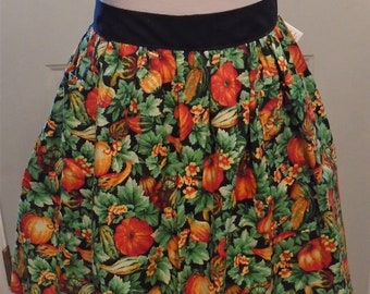 May include: A knee-length skirt with a black waistband and a vibrant print featuring pumpkins, gourds, and foliage in shades of orange, green, and yellow against a black background. The skirt has a full, gathered design.