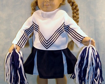 May include: A doll wearing a white and navy blue cheerleader outfit, holding navy and white pom-poms. The outfit includes a white top with black stripes, a navy skirt with white accents, and white trainers. The doll has blonde hair in plaits.
