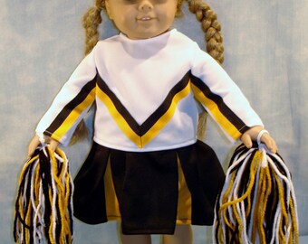 May include: A doll in a cheerleader outfit, featuring a white top with black and gold detailing, a black skirt with gold trim, and white trainers. The doll has blonde plaits and holds black, gold, and white pom-poms.