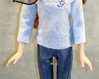 May include: A fashion doll wearing a light blue terrycloth sweater with a cursive "G" embroidered on the chest, paired with denim capri pants and white ankle boots. A patterned scarf is draped around the neck.