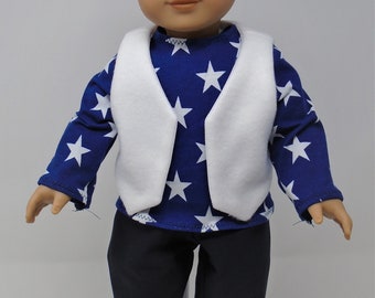 May include: A doll wearing a blue shirt with white stars, a white vest, black pants, and black shoes. The doll has dark hair and is standing against a white background. The doll's outfit resembles a patriotic theme.