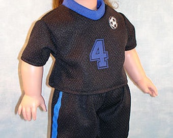 Puede incluir: Una muñeca vestida con un uniforme de fútbol negro con detalles azules, que incluye una camiseta con el número 4, pantalones cortos y calcetines. La muñeca está de pie sobre un balón de fútbol. La muñeca tiene cabello castaño y lleva un uniforme de fútbol azul y negro.