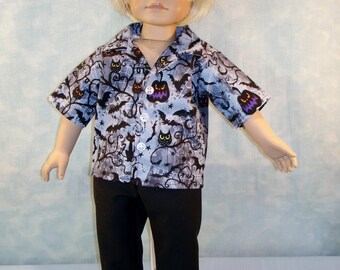 May include: A doll wearing a Halloween-themed outfit. The short-sleeved button-down shirt features a pattern of bats, cats, and jack-o'-lanterns on a light blue background. The doll is also wearing black pants and black shoes. The doll has blonde hair and blue eyes.