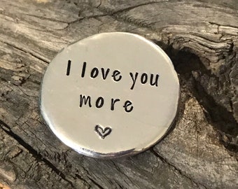 May include: Silver round charm with the text "I love you more" and a small heart.