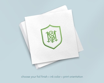 May include: White square napkins stacked, with a green shield-shaped monogram design. The monogram features the letters "MS" in an ornate, stylized font. The text at the bottom reads "choose your foil finish + ink color + print orientation."