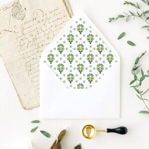 May include: A white envelope with a green floral pattern lining. The image also includes a vintage letter, wax seals, a wax melting spoon, and a floral stamp, all arranged on a white surface. The overall theme is stationery and correspondence.