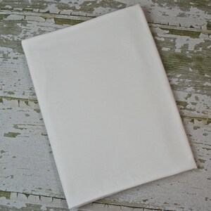 May include: A plain white fabric swatch, shown on a weathered wooden surface.