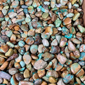 May include: A close-up view of a collection of turquoise stones. The stones are various shades of blue, green, and brown. They are smooth and polished, and they have a natural, organic look.