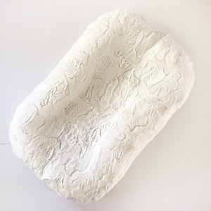 May include: A white, rectangular baby nest with a textured, plush surface. The nest is designed with rounded edges and a soft, inviting appearance, perfect for newborns. The overall color is a creamy white.