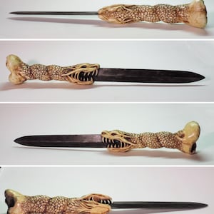 Puede incluir: Un cuchillo decorativo con un mango de cabeza de dragón. El mango está hecho de un material marrón claro y tiene una superficie texturizada. La hoja es plateada y tiene una punta afilada.