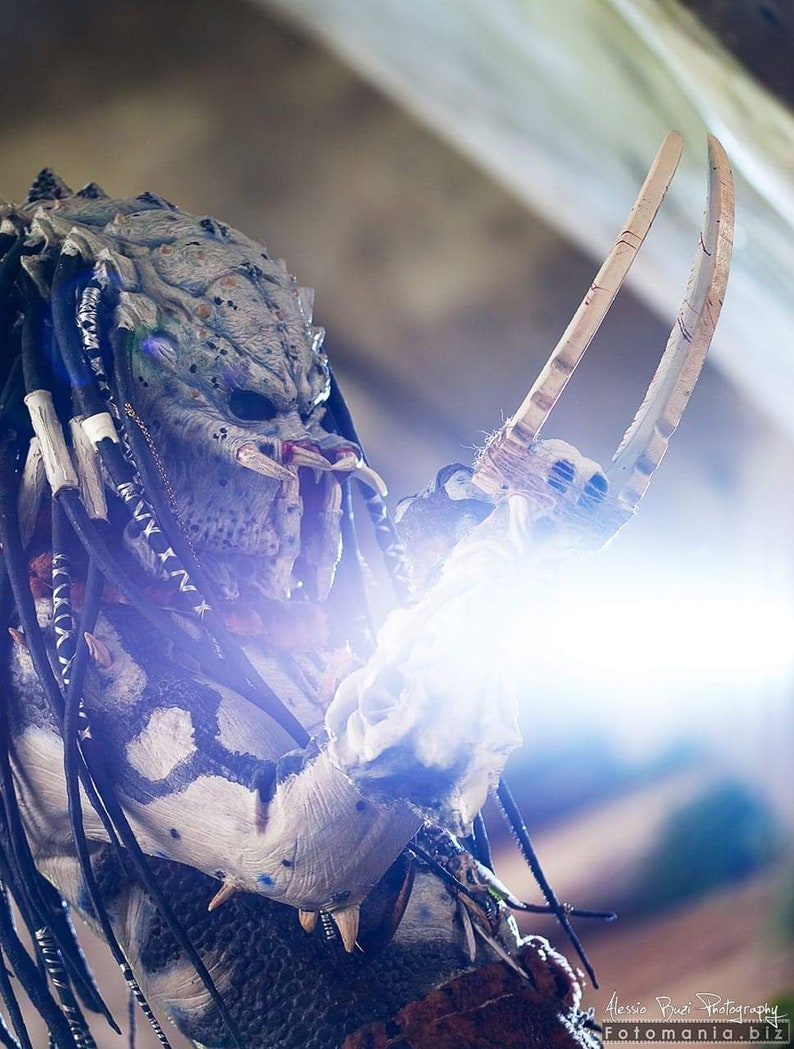 Pu&ograve; includere: Un costume da Predator con un designo a motivi bianco e nero. Il costume presenta una maschera con una mascella appuntita e una lunga treccia di dreadlocks bianchi e neri che fluiscono. Il Predator tiene un paio di lame lunghe e affilate.