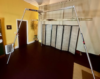 May include: A silver metal frame with a wooden bar suspended from it. The frame is freestanding and has adjustable height. The frame is in a room with a wooden floor and a bamboo screen.