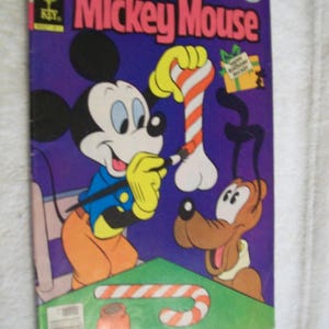 May include: A vintage comic book cover featuring Mickey Mouse and Pluto. Mickey is wearing a blue shirt and orange pants, holding a candy cane. Pluto is sitting at a table with a candy cane and a bowl. The cover is purple with the text "Walt Disney's Mickey Mouse" in pink and white.