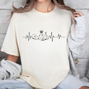 May include: A white t-shirt with a black snake design and a heartbeat graphic. The text "IVORY XL" is visible in the bottom right corner of the image.